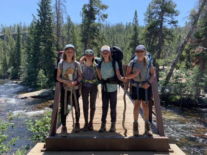 Four middle school aged students with backpacks standing on a bridge in the mountains